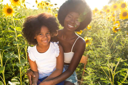 Beautiful afro-american mom and daughter palying and having fun in a sunflowers fieldの写真素材