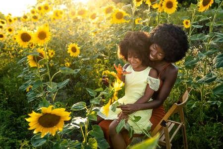 Beautiful afro-american mom and daughter palying and having fun in a sunflowers fieldの写真素材