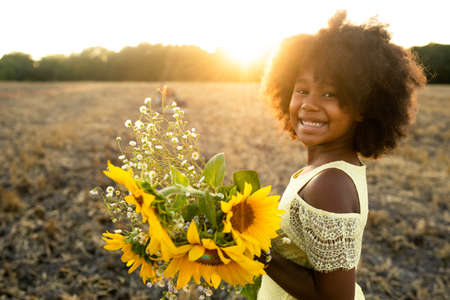 Pretty afro american girl in a sunflowers field having funの写真素材