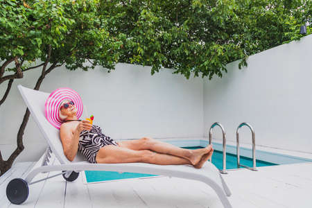 Happy senior woman having party in the swimming pool - Beautiful senior lady sunbathing and relaxing...