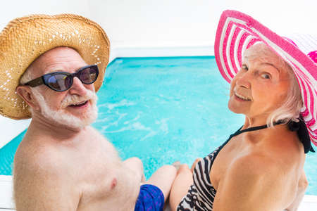 Happy senior couple having party in the swimming pool - Elderly friends releaxing at a pool party during summer vacationの写真素材