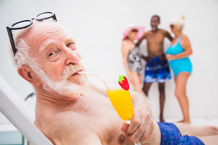 Happy senior man having party in the swimming pool - Active elderly male person sunbathing and relaxing in a private pool during summertimeの写真素材