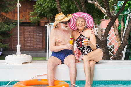 Happy senior couple having party in the swimming pool - Elderly friends releaxing at a pool party during summer vacationの写真素材