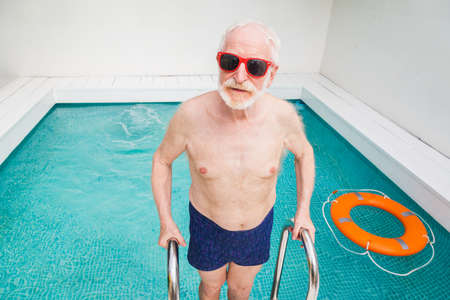 Happy senior man having party in the swimming pool - Active elderly male person sunbathing and relaxing in a private pool during summertimeの写真素材