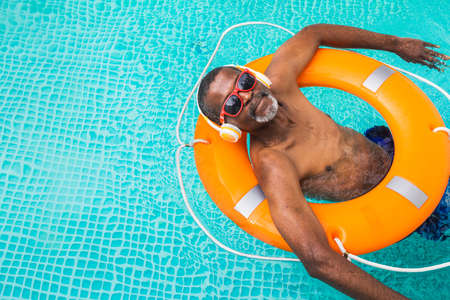 Happy senior man having party in the swimming pool - Active elderly male person sunbathing and relaxing in a private pool during summertimeの写真素材