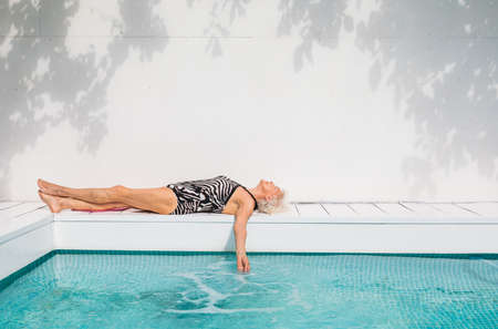 Happy senior woman having party in the swimming pool - Beautiful senior lady sunbathing and relaxing in a private pool during summertimeの写真素材