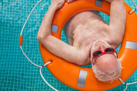 Happy senior man having party in the swimming pool - Active elderly male person sunbathing and relaxing in a private pool during summertimeの写真素材