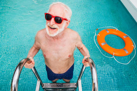 Happy senior man having party in the swimming pool - Active elderly male person sunbathing and relaxing in a private pool during summertimeの写真素材