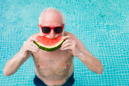 Happy senior man having party in the swimming pool - Active elderly male person sunbathing and relaxing in a private pool during summertimeの写真素材