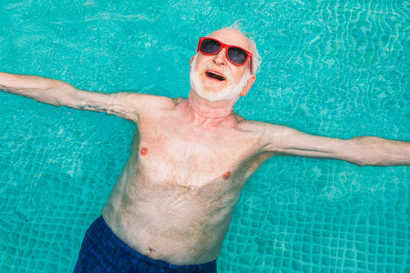 Happy senior man having party in the swimming pool - Active elderly male person sunbathing and...
