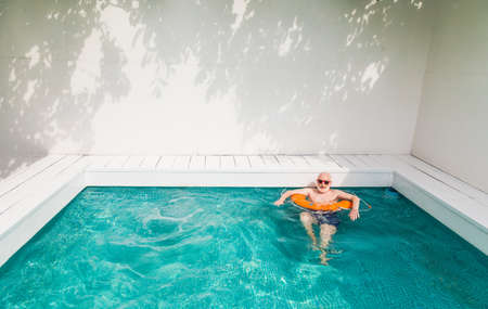 Happy senior man having party in the swimming pool - Active elderly male person sunbathing and relaxing in a private pool during summertimeの写真素材
