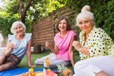 Beautiful senior women relaxing at home in the garden - Three pretty mature ladies rest in a peaceful backyard gardenの写真素材