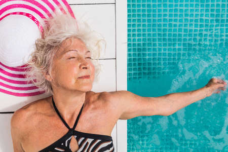 Happy senior woman having party in the swimming pool - Beautiful senior lady sunbathing and relaxing...