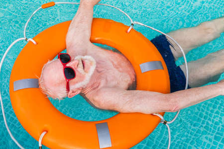 Happy senior man having party in the swimming pool - Active elderly male person sunbathing and relaxing in a private pool during summertimeの写真素材