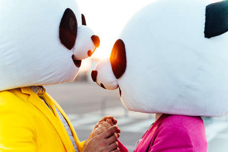 Image of friends wearing giant panda head and colored suits. Colored mascots making party