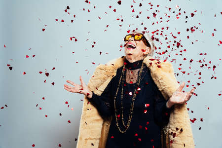 image of a beautiful and elegant old influencer woman. Cool grandmother posing in studio wearing fashionable clothes. Confetti explosion on her 90s birthday celebrationの写真素材