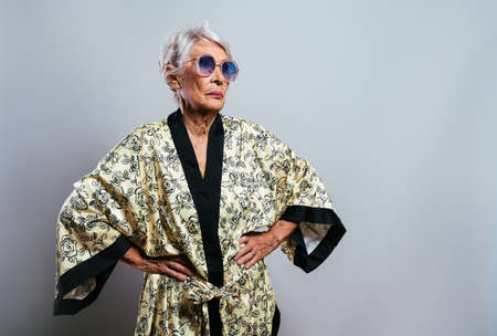 beautiful and elegant old influencer woman. Cool grandmother posing in studio wearing fashionable clothes. Happy senior lady celebrating and making party. Concept about seniority and lifestyleの写真素材