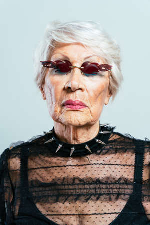 beautiful and elegant old influencer woman. Cool grandmother posing in studio wearing fashionable clothes. Happy senior lady celebrating and making party. Concept about seniority and lifestyleの写真素材