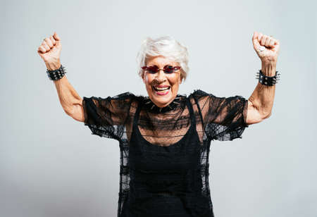 beautiful and elegant old influencer woman. Cool grandmother posing in studio wearing fashionable clothes. Happy senior lady celebrating and making party. Concept about seniority and lifestyleの写真素材