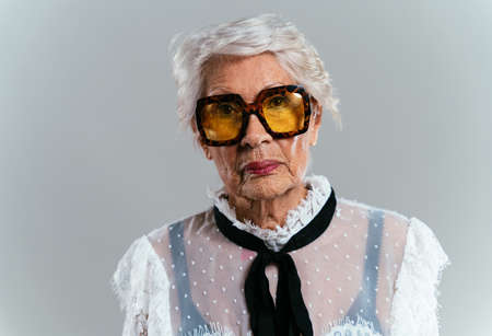 beautiful and elegant old influencer woman. Cool grandmother posing in studio wearing fashionable clothes. Happy senior lady celebrating and making party. Concept about seniority and lifestyleの写真素材