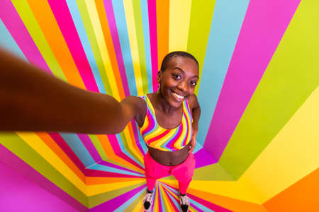 Beautiful african american young woman dancer having fun inside a rainbow box room - Cool and stylish afro adult woman portrait on multicolored background, influencer creating content for social networks in a selfie roomの写真素材
