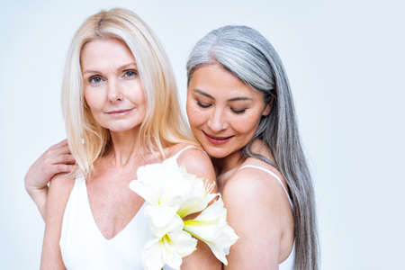 beauty image of two women with different age, skin and body posing in studio for a body positive photoshooting. Mixed female models in lingerie on colored backgroundsの写真素材