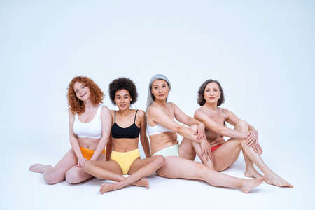 Beauty image of a group of women with different age, skin and body posing in studio for a body positive photoshooting. Mixed female models in lingerie on colored backgroundsの写真素材