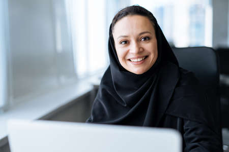 beautiful woman with abaya dress working on her computer. Middle aged female employee at work in a business office in Dubai. Concept about middle eastern cultures and lifestyleの写真素材