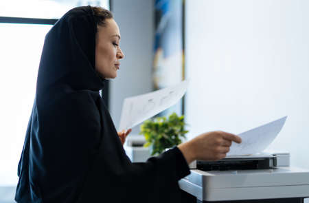beautiful woman with abaya dress working and printing documents. Middle aged female employee at work...