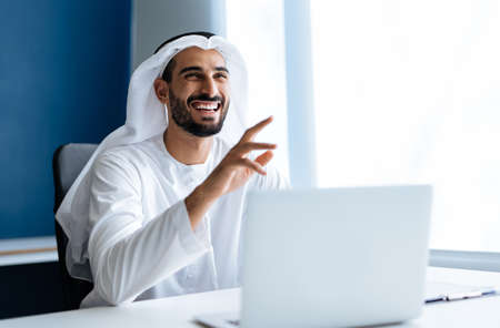 Handsome man with dish dasha working in his business office of Dubai. Portraits of a successful businessman in traditional emirates white dress. Concept about middle eastern cultures, lifestyle and professional occupationsの写真素材