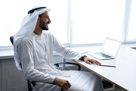 Handsome man with dish dasha working in his business office of Dubai. Portraits of a successful businessman in traditional emirates white dress. Concept about middle eastern cultures, lifestyle and professional occupationsの写真素材
