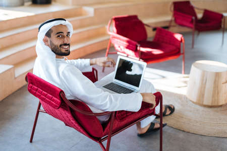 handsome man with dish dasha working in his business office of Dubai. Portraits of a successful businessman in traditional emirates white dress. Concept about middle eastern cultures, lifestyle and professional occupationsの写真素材