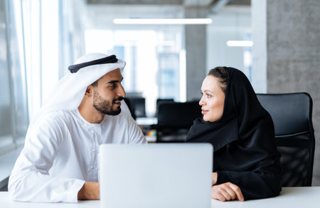 Man and woman with traditional clothes working in a business office of Dubai. Portraits of successful entrepreneurs businessman and businesswoman in formal emirates outfits. Concept about middle eastern cultures, lifestyle and professional occupationsの写真素材