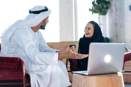 Man and woman with traditional clothes working in a business office of Dubai. Portraits of successful entrepreneurs businessman and businesswoman in formal emirates outfits. Concept about middle eastern cultures, lifestyle and professional occupationsの写真素材