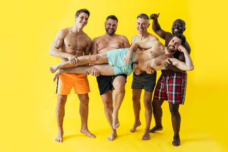 group of multiethnic men posing for a male edition body positive beauty set. guys with different age, and body wearing trunks swimwear ready to go at the beachの写真素材