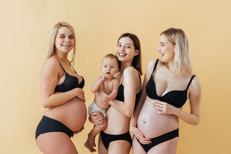 Happy pregnant woman with big belly on colored background - Young woman wearing underwear expecting a baby - Pregnancy, motherhood, people and expectation concept -の写真素材