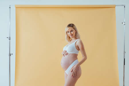 Happy pregnant woman with big belly on colored background - Young woman wearing underwear expecting...