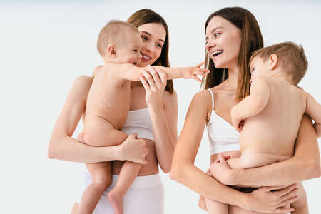 Happy women holding their babies on colored background - Young women wearing underwear taking care of their little sons - Pregnancy, motherhood, people and expectation conceptの写真素材