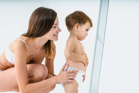 Happy woman holding her baby on colored background - Young woman wearing underwear taking care of her little son - Pregnancy, motherhood, people and expectation conceptの写真素材