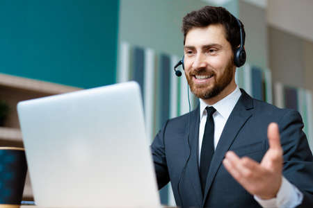 Businessman with elegant suit sitting at computer desk in the office and joining in a video...