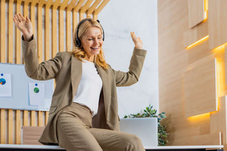 Beautiful and cheerful mature adult senior woman standing in the office - Portrait of successful corporate businesswoman with formal elegant dress listening music and singing, leisure and funny moments at workの写真素材