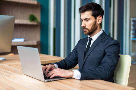 Businessman with elegant suit sitting at computer desk in the office - Adut man working at laptop...