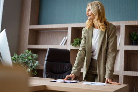 Beautiful mature adult businesswoman with elegant dress sitting at computer desk in the office - Senior woman working at pc online, concepts about business and technologyの写真素材