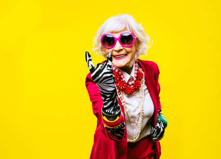 Happy and funny cool old lady with fashionable clothes portrait on colored background - Youthful...