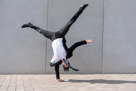 Happy and handsome adult businessman wearing elegant suit doing acrobatic trick moves in the city,...