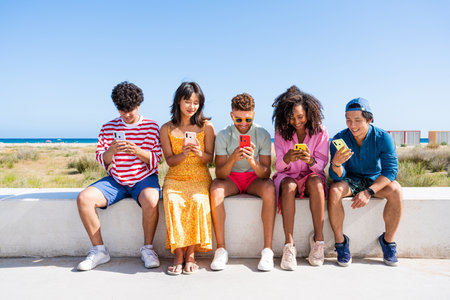 Multiethnic group of young happy friends bonding outside, having fun on summertime vacation - Multicultural cheerful people with summer clothes using mobile phones, concepts about youth, friendship and communication technologyの写真素材
