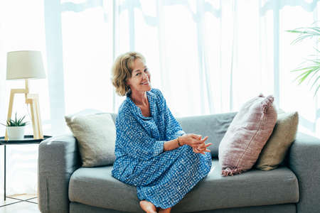 Beautiful mature senior woman at home, domestic life and leisure moments - 50-60 years old pretty female adult relaxing on the sofaの写真素材