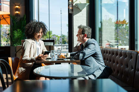 Senior businessman and beautiful hispanic businesswoman meeting in a bar restaurant - Two colleagues bonding in a cafe after workの写真素材