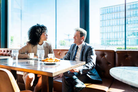 Senior businessman and beautiful hispanic businesswoman meeting in a bar restaurant - Two colleagues bonding in a cafe after workの写真素材