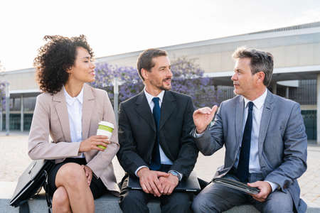Multiracial group of business people bonding outdoors - International business corporate team wearing elegant suit meeting in a business parkの写真素材